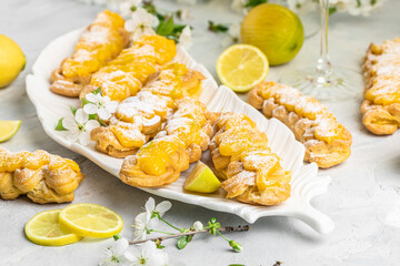Eclairs with lemon curd topping on serving plate with glass of limoncello on a light background,...