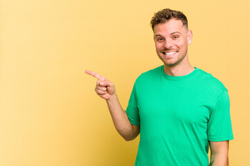 Young caucasian handsome man isolated on yellow background smiling cheerfully pointing with forefinger away.