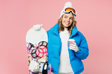 Snowboarder woman wear blue suit goggles mask hat ski padded jacket hold takeaway paper cup coffee to go look aside isolated on plain pink background. Winter extreme sport hobby weekend trip concept.