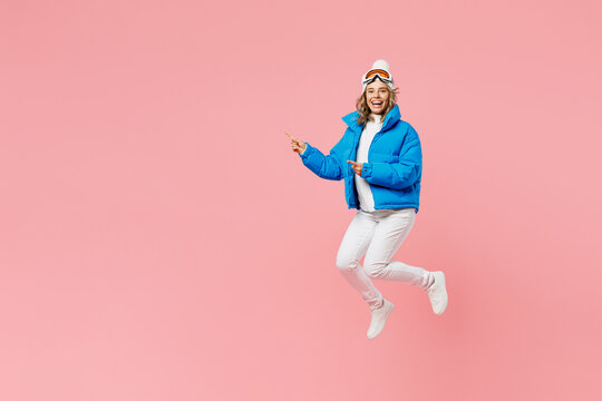 Snowboarder Fun Woman Wear Blue Suit Goggles Mask Hat Ski Padded Jacket Jump Point Finger Aside On Area Isolated On Plain Pastel Pink Background. Winter Extreme Sport Hobby Weekend Trip Relax Concept.