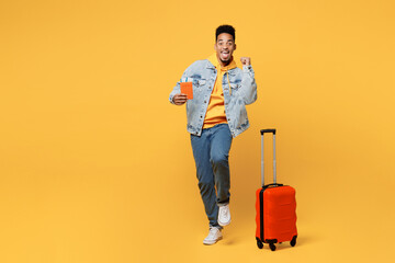 Full body traveler man of African American ethnicity in casual clothes hold valise passport ticket isolated on plain yellow background Tourist travel abroad in free time rest Air flight trip concept