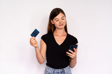 Confident young woman holding smartphone and credit card. Portrait of Caucasian lady wearing black T-shirt and jeans using cashless payment in online shop. Contactless payment concept
