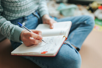 Free time you need to do something, woman unrecognizable sits on floor of room, in chair, writes in...