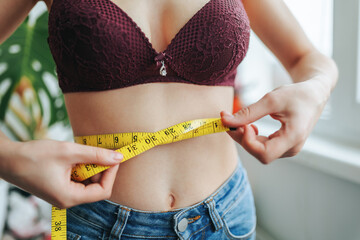 Unrecognizable young girl woman on diet measures her waist with centimeter tape. Woman hands hold centimeter tape. Result is unknown. Close up. Beauty and weight loss concept - obrazy, fototapety, plakaty
