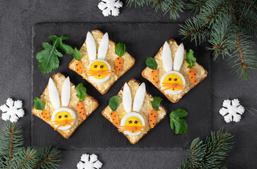 Obraz na płótnie Canvas Sandwiches for the New Year 2023 of canned tuna, eggs and melted cheese, decoration bunny from egg on slate board