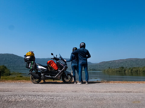 Chaiyaphum, Thailand - December 21, 2019: young traveler couple stand next to Yamaha Nmax scooter loaded with luggage for holiday trip. Park and view the view by the reservoir, motorcycle camping