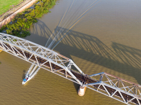 Aerial view of a speed boat going under a steel bridge crossing a wide brown river