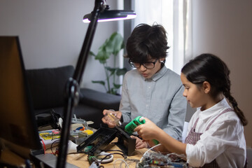 School children studying robotics. Boy holding light bulb, girl using hot glue gun, they working on school project. Education, hobby and robotics concept