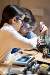 Focused school boy in protective glasses using screwdriver to fix elements in new electronic device. Girl helping him. Electronics, hobby concept