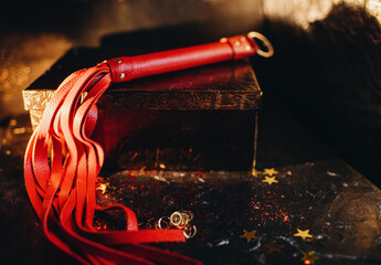 bdsm toys, red leather whip on a black background with red glitter