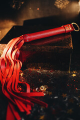 bdsm toys, red leather whip on a black background with red glitter