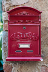 Traditional red colored old mailbox hanging on the wall in Italian countryside.
