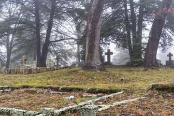 Early foggy morning in an old hill top graveyard with trees and moss covered headstones, rock wall and crosses. Autumn leaves covering the ground in Sewanee Tennessee university cemetery.