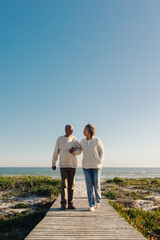 Retired elderly couple walking down a foot bridge at the beach