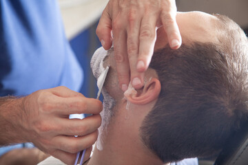 Obraz na płótnie Canvas Hands of barber holding razor and shaving a client.