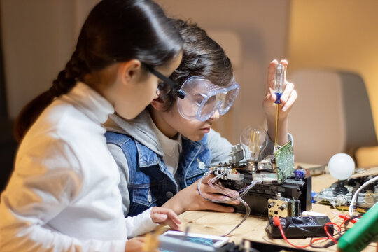 Concentrated boy in protective glasses using screwdriver to fix elements in new electronic device. Girl helping him, giving advice. Electronics, hobby concept