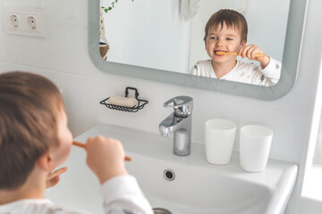 Cute male kid in pajamas cleaning teeth with eco friendly toothbrush comfortable minimalist bathroom