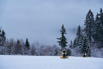 Winter mountains panorama with snow cannons, ski slopes and ski lifts among spruce forest on a...