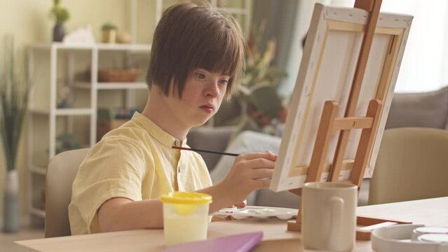 Creative girl with down syndrome painting on canvas at home