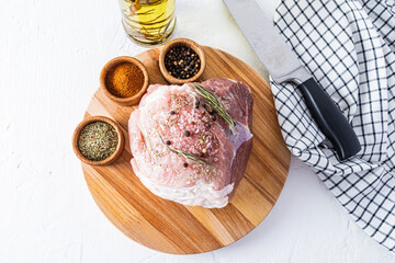a large fresh piece of pork for baking lies on a round wooden board with various spices. top view. white background.