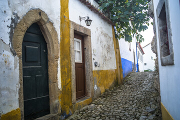 Fototapeta na wymiar Narrow cobblestone streets, historic white houses covered with ceramic tiles, townhouses and the castle of the town of Obidos.