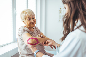 Female physiotherapists provide assistance to senior female patients with elbow injuries examine...