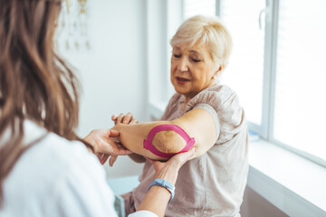 Kinesiology taping treatment with pink tape on senior patient injured arm. Woman hands apply...