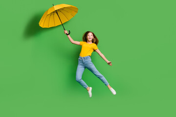 Full size portrait of overjoyed cheerful girl jumping arm hold umbrella isolated on green color background © deagreez