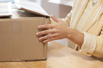 Unrecognizable woman preparing box for shipping. Closeup of postal worker in jacket checking cardboard box. Logistics concept