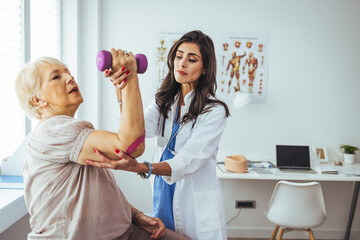Physiotherapist helping senior woman with elbow exercise in clinic. Doctor checking elbow of senior...