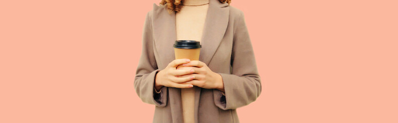 Close up of female hands holding cup of coffee wearing coat on beige background