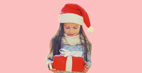 Christmas portrait of happy smiling little girl child in santa red hat with gift box on pink background