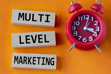 MULTI LEVEL MARKETING - words on wooden blocks on orange background with red clock