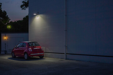 Obraz na płótnie Canvas 白い壁際に駐車された赤い車を照らすライト 