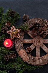 wiccan altar with Wheel of the year, candle, amulet deer, cones, fir branches on dark abstract...