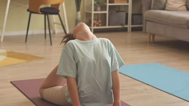 Girl with down syndrome arching back to make her feet touch her head while doing stretching exercises on mat at home