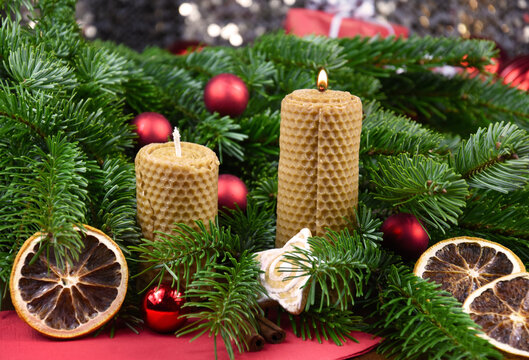 Beeswax candles and fir branch christmas decoration stock images. Beautiful rustic christmas still life stock photo. Burning candle, dried orange and red Christmas balls images