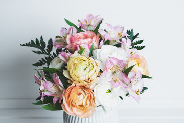 Beautiful bouquet of fresh colorful pastel ranunculus and lily flowers in full bloom with green fern leaves in vase against white background, close up. Spring bunch of blossoms.