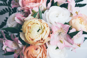 Beautiful bouquet of fresh colorful pastel ranunculus and lily flowers in full bloom with green fern leaves against white background, close up. Floral backdrop.