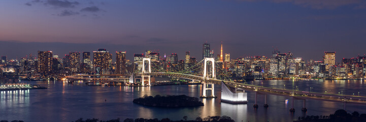 Wide panorama image of Tokyo cityscape at dusk with Rainbow bridge and Tokyo tower.