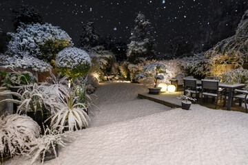 Beautiful landscaped English garden at night in snow lit by stylish, designer, garden lights.
