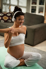 Fototapeta na wymiar Beautiful pregnant woman practising yoga at home. Young woman listening music while exercise at home