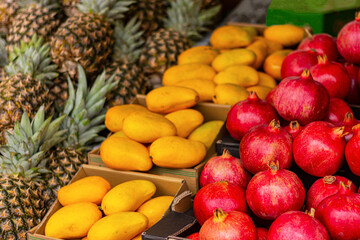 close up of pineapples, mangoes and pomegranates on counter in market. textured background of natural fruits