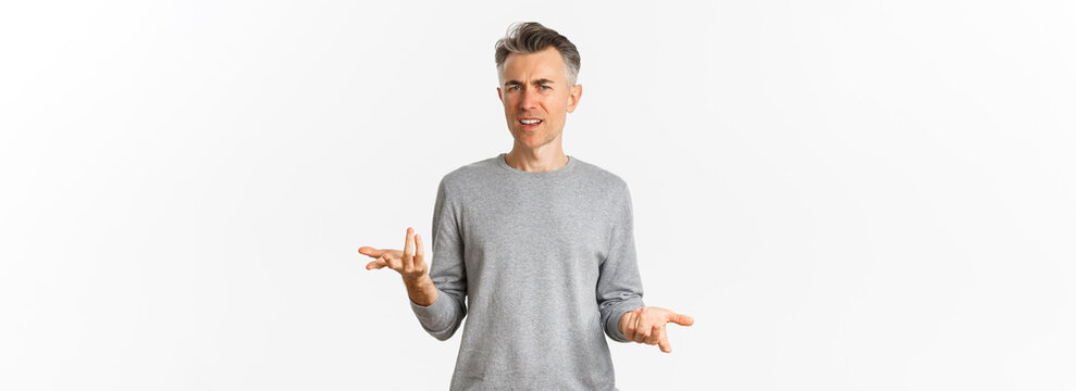 Portrait of confused and disappointed middle-aged man arguing, cant understand something and asking why, standing over white background perplexed