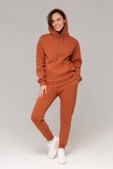 Smiling woman with thick curly hair in a brown suit of hoodies and sweatpants. Mock-up.