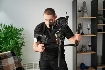 Videographer man shooting footage indoors, using camera mounted on gimbal stabilizer equipment.