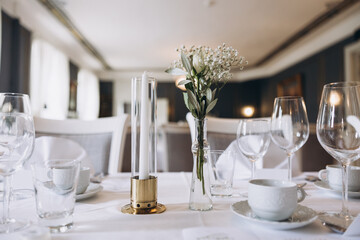 Wedding. Banquet. On festive tables with white tablecloths there are compositions of flowers, candles, cutlery, glasses, plates, menu cards and name plates