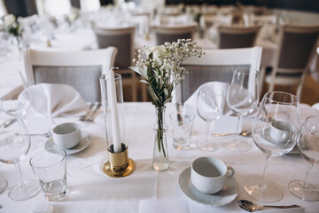 Wedding. Banquet. On festive tables with white tablecloths there are compositions of flowers, candles, cutlery, glasses, plates, menu cards and name plates