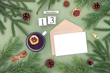 December 13. Calendar date, white blank with craft envelope, cup of tea and natural decor on green background. Hello winter. Template for your design, greeting card