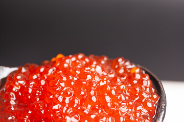 Delicious red caviar in wooden spoon on black white background